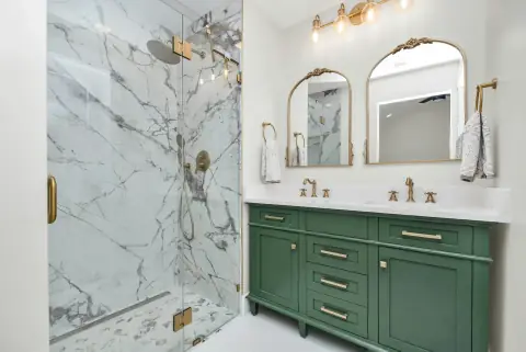 Green-painted vanity under arched mirrors in a marble-tiled bathroom.