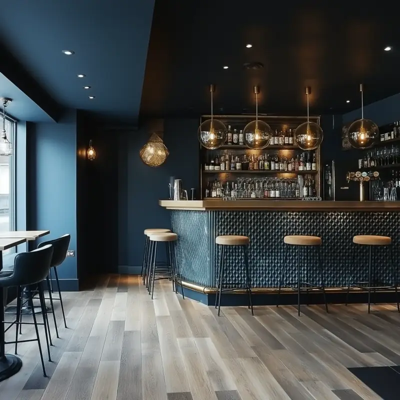 Refurbished bar with deep blue walls, a tiled bar front, brass stools and globe pendant lights.
