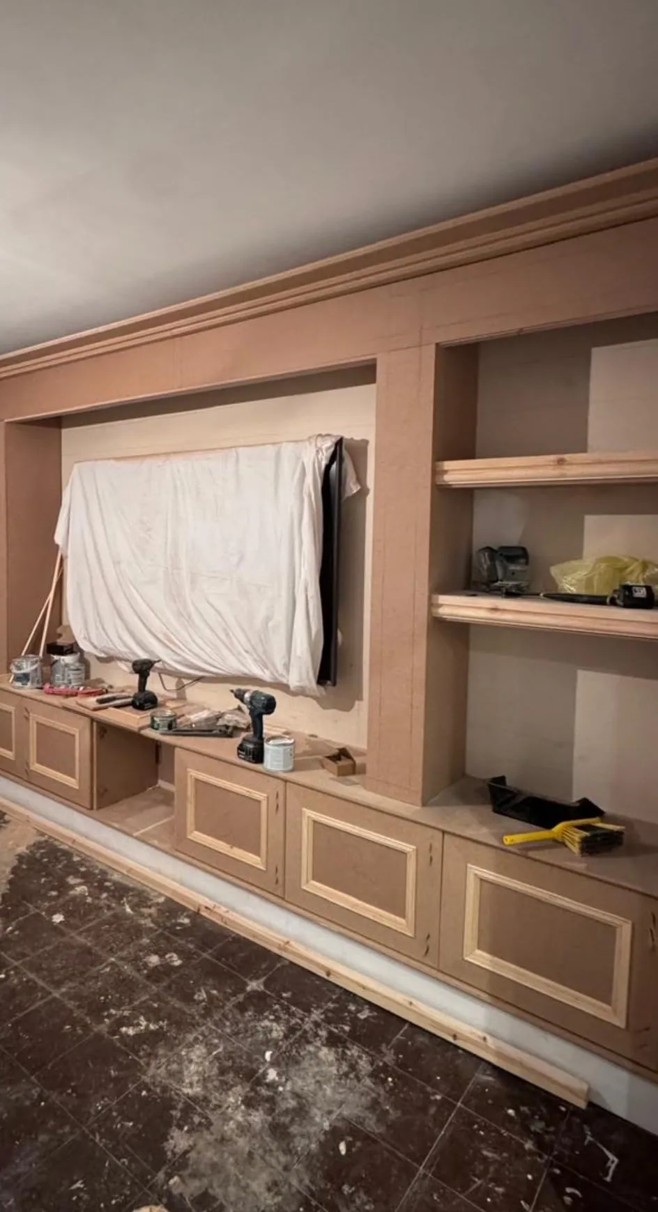 A built-in media wall being made up in MDF, with the television recess sheeted over, open shelves alongside and tools still on the worktop.