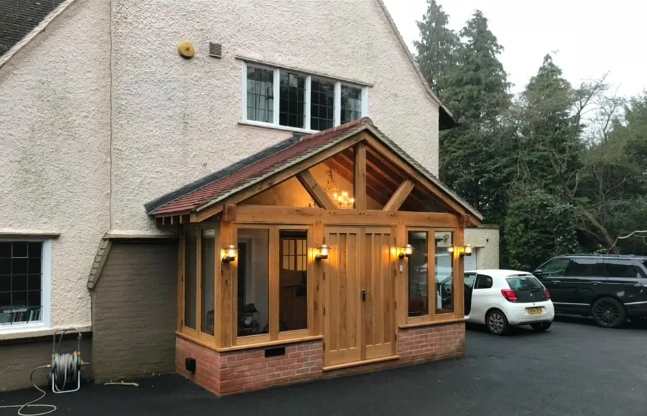 A green-oak porch with glazed sides and a clay-tiled roof, built onto the front of a rendered house.