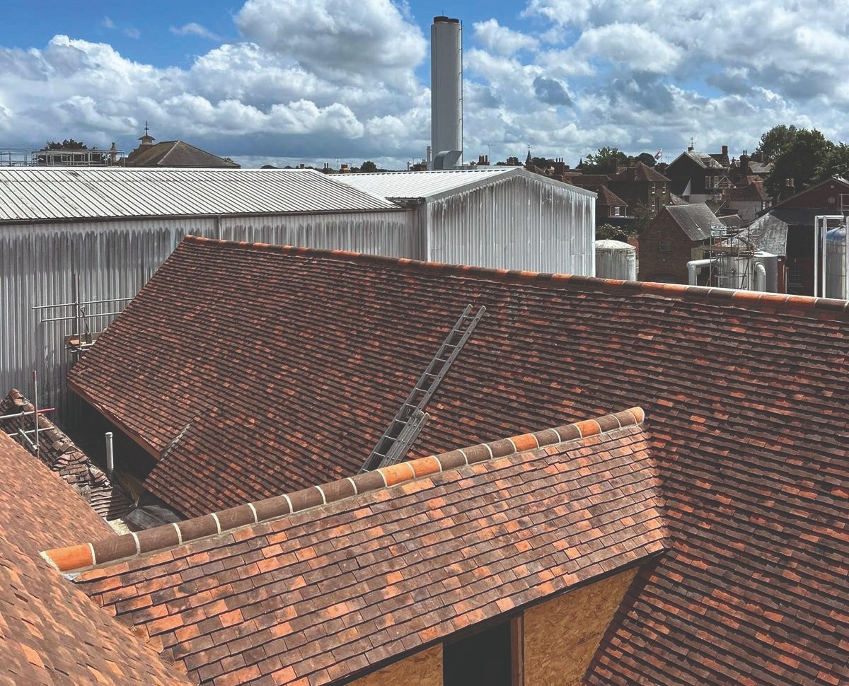 The re-roofed brewery buildings at Shepherd Neame's Faversham Brewery, in handmade Kent clay plain tiles with half-round ridge tiles, the brewery chimney behind.