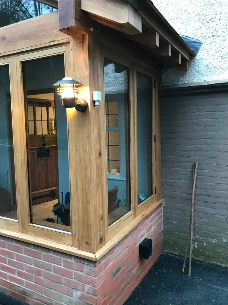 A new oak-framed porch with glazing on a red brick dwarf wall, built onto the corner of a house.