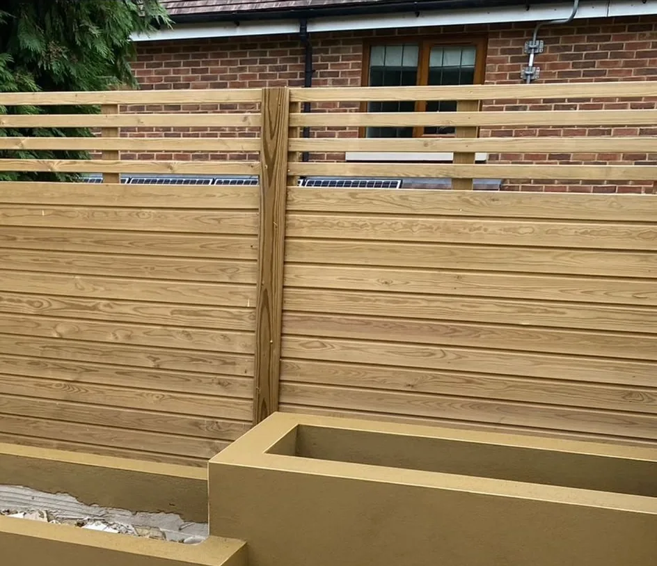 A rendered raised planter and low garden wall finished in olive render, with a new slatted timber fence and trellis top behind, still on dust sheets mid-job.