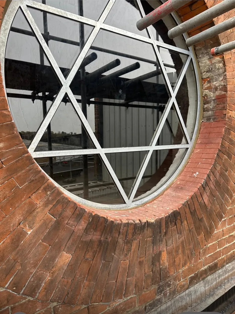 A restored circular rose window with steel tracery in a red brick gable, with scaffolding up and the new steel frame visible inside.
