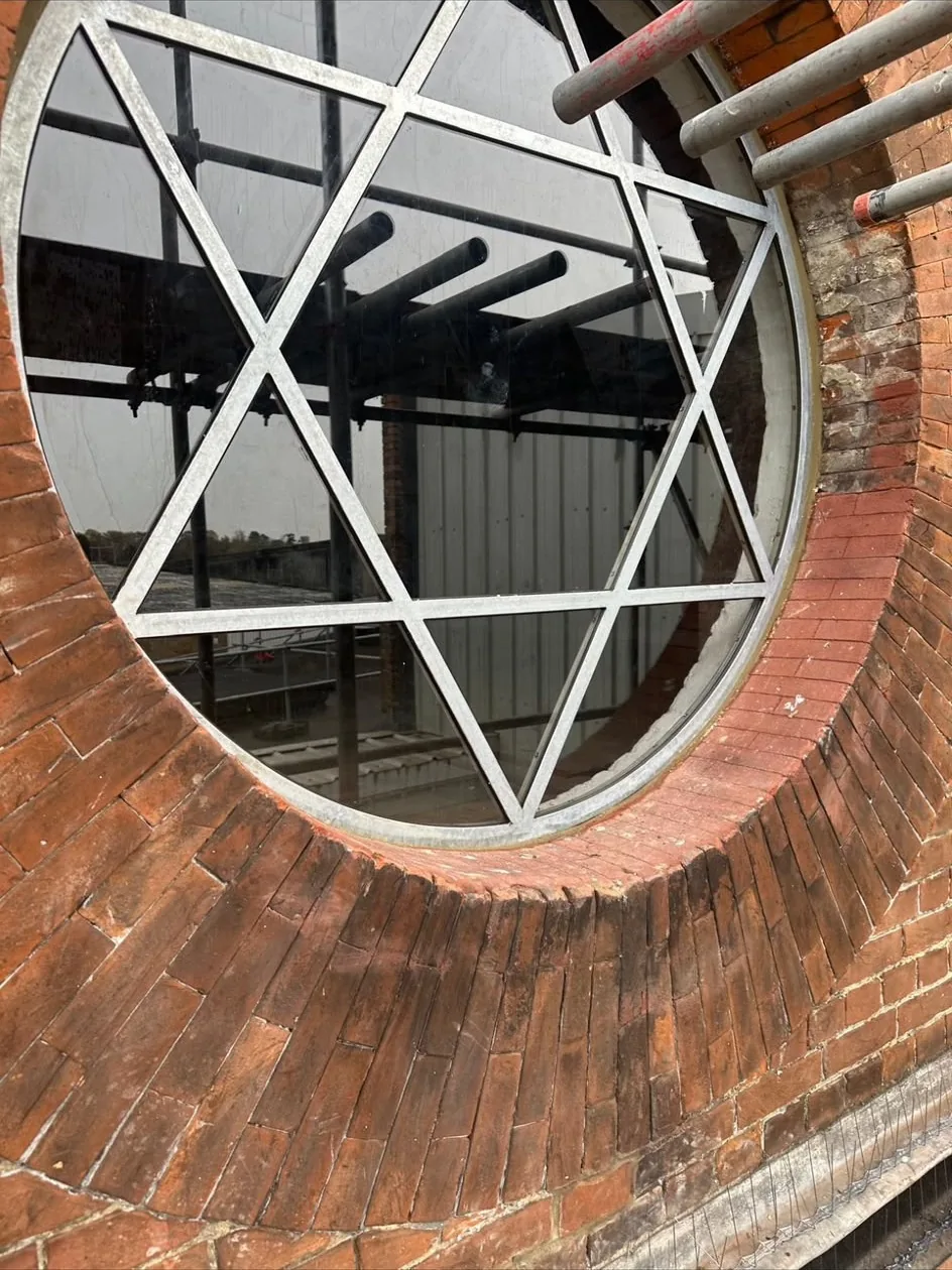 Circular brick window with steel star glazing bars set into a rebuilt red brick elevation, with scaffolding still up alongside.