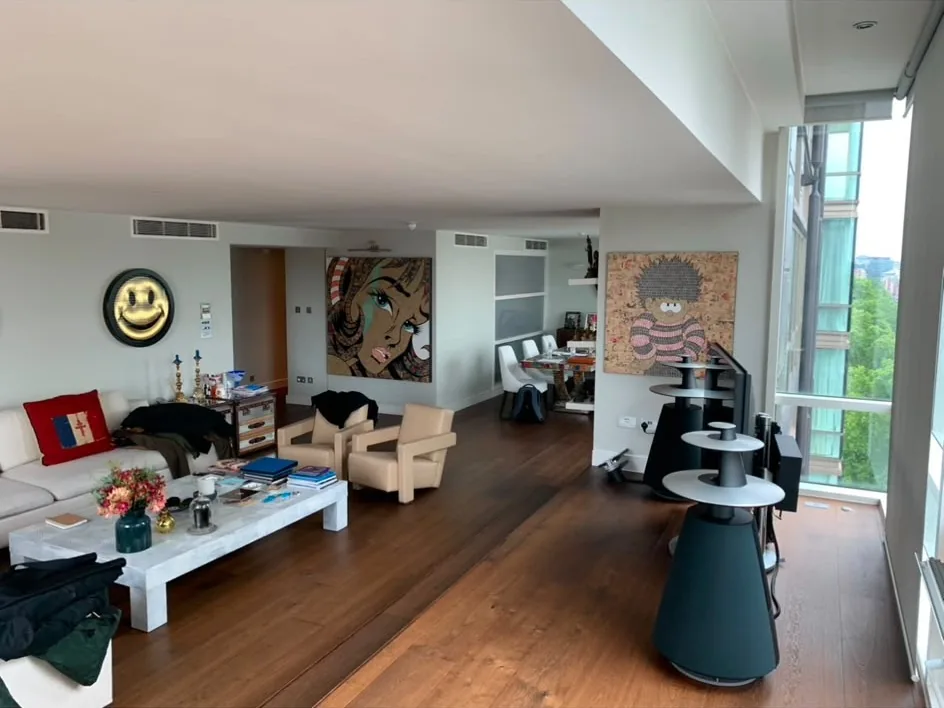 Finished open-plan living area in a refurbished flat, with wide oak boards, a white corner sofa and full-height glazing along one side.