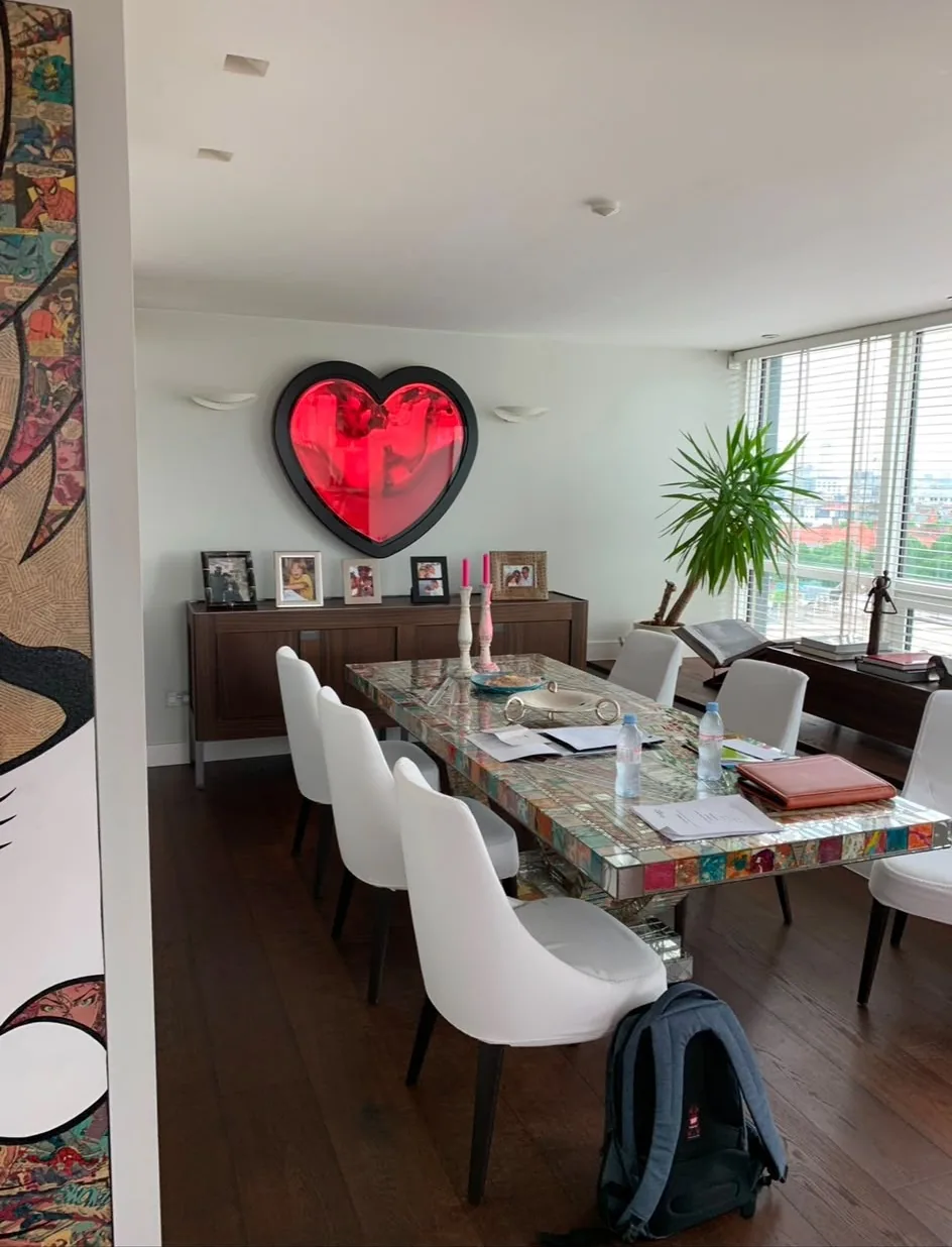 A dining room with white chairs round a long table, dark timber flooring and full-height windows, art on every wall.
