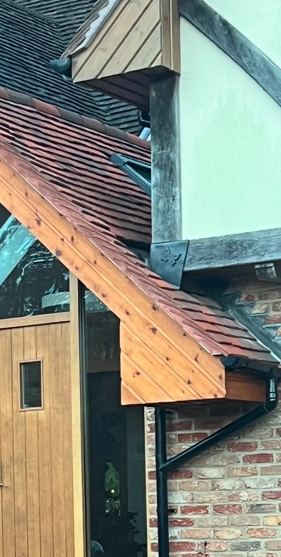 A finished roof junction with clay tiles, oak bargeboards and leadwork where the lower pitch meets the render.