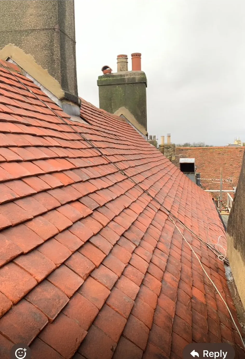 A newly tiled clay plain-tile roof with fresh leadwork where the slope meets the rendered chimney stack.