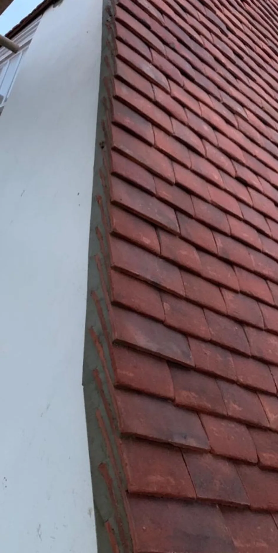 Newly laid red clay plain tiles on a pitched roof, with the mortar-bedded verge finished against a white rendered wall.