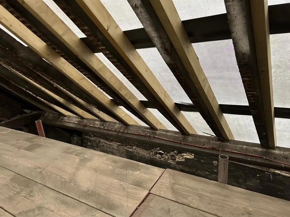 New rafters sistered to the original roof timbers with breathable membrane and battens above, and a red pipe run along the wall plate.