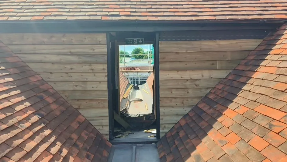 New clay plain tiles laid to both slopes either side of a valley, with timber cladding and a black-framed opening between them.