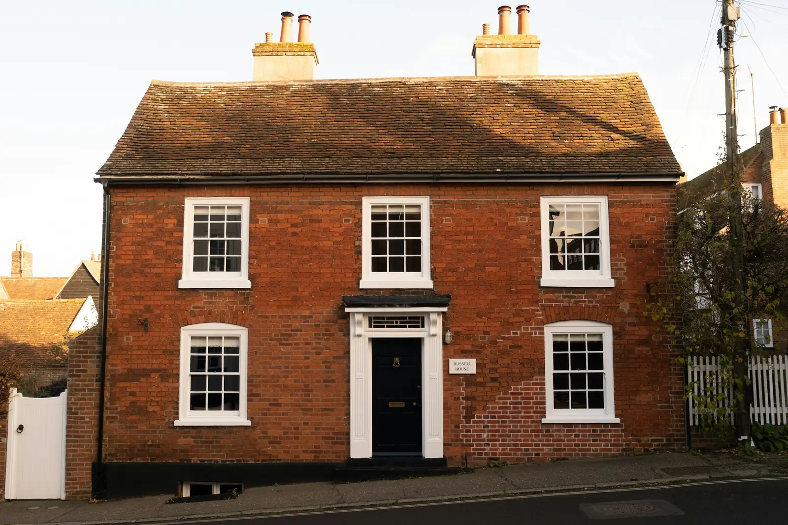 A red brick Georgian house with crisp white sash windows, a navy panelled front door and a clay tiled roof.
