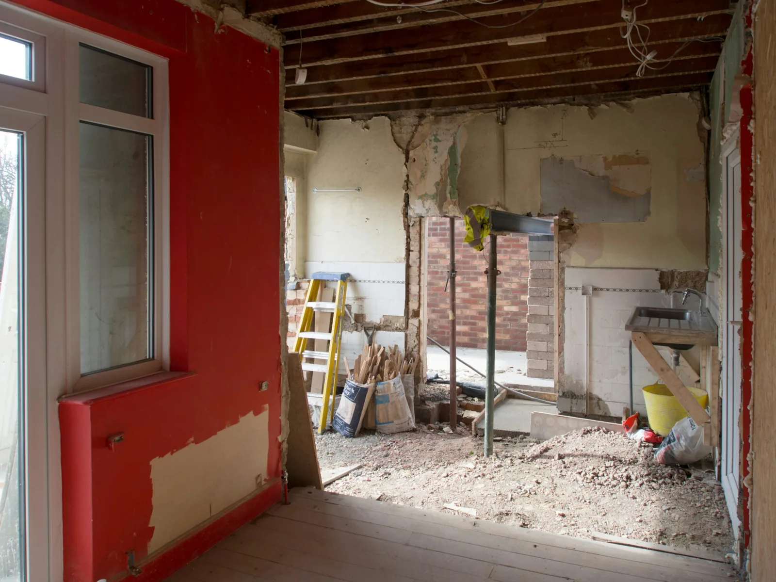 Steel beam on acrow props holds the knocked-through opening, joists bare above the rubble.