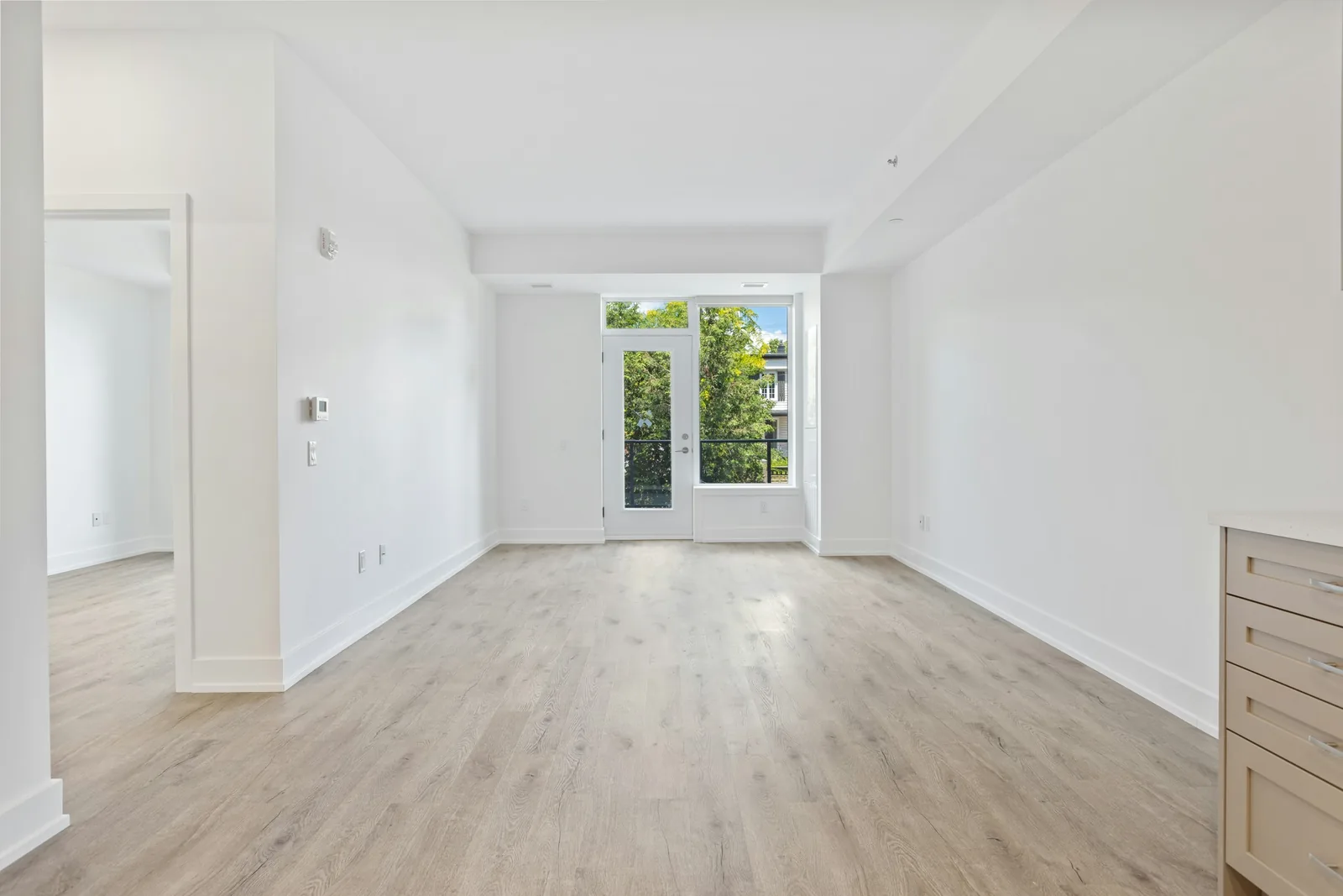 Pale boards lead across an empty white room to a glazed door with a guard rail behind it.