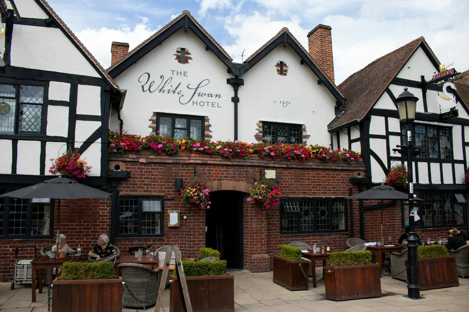 A long window box of flowers runs across the brick front of a black-and-white pub.