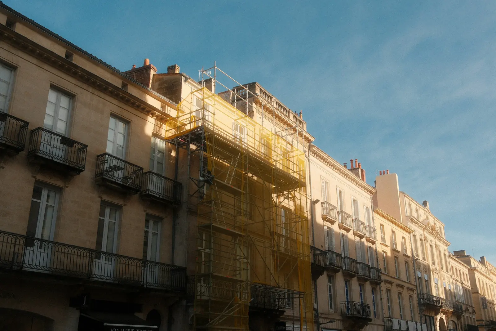 Yellow netting covers the scaffold on a single building in a stone terrace of iron balconies.