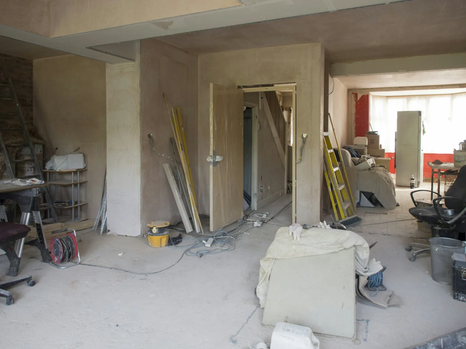 Newly plastered walls and a fresh door lining, with ladders, a cable reel and offcuts still out.