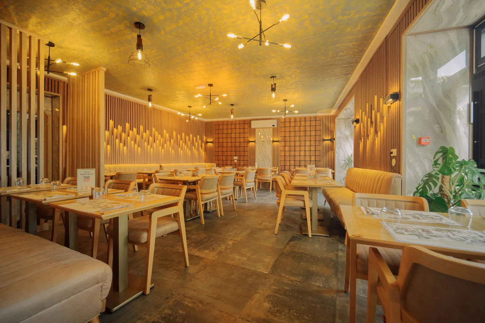 Gold-painted ceiling over slatted timber walls, cream banquettes and pale timber tables on tiles.
