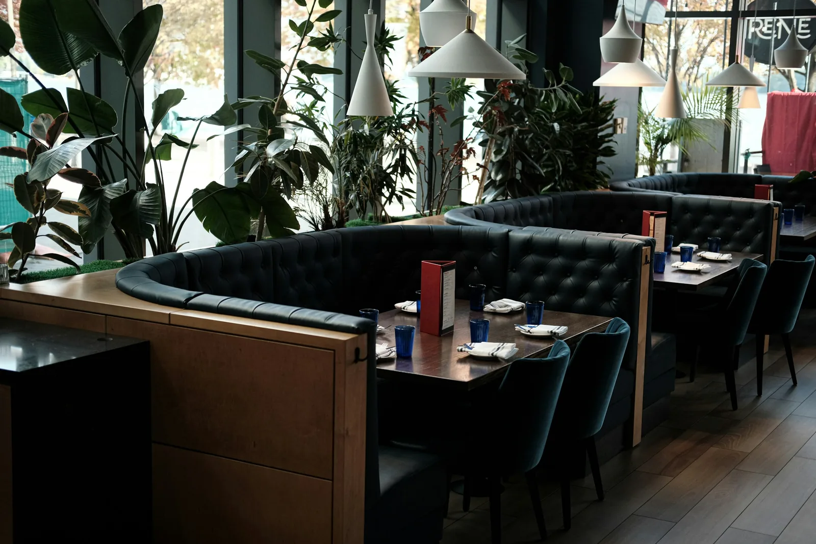 A curved buttoned banquette wraps a laid table of blue tumblers and folded napkins.