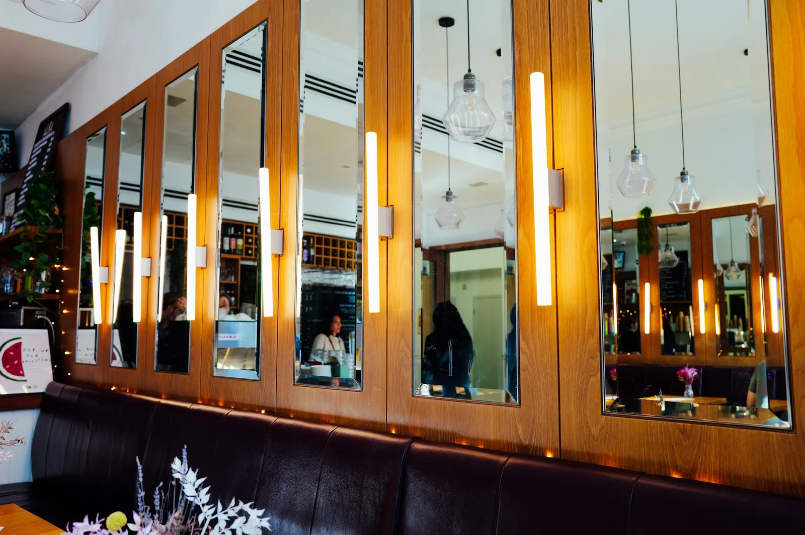 Mirror panels and slim tube lights fill a timber-panelled wall above a dark leather bench.
