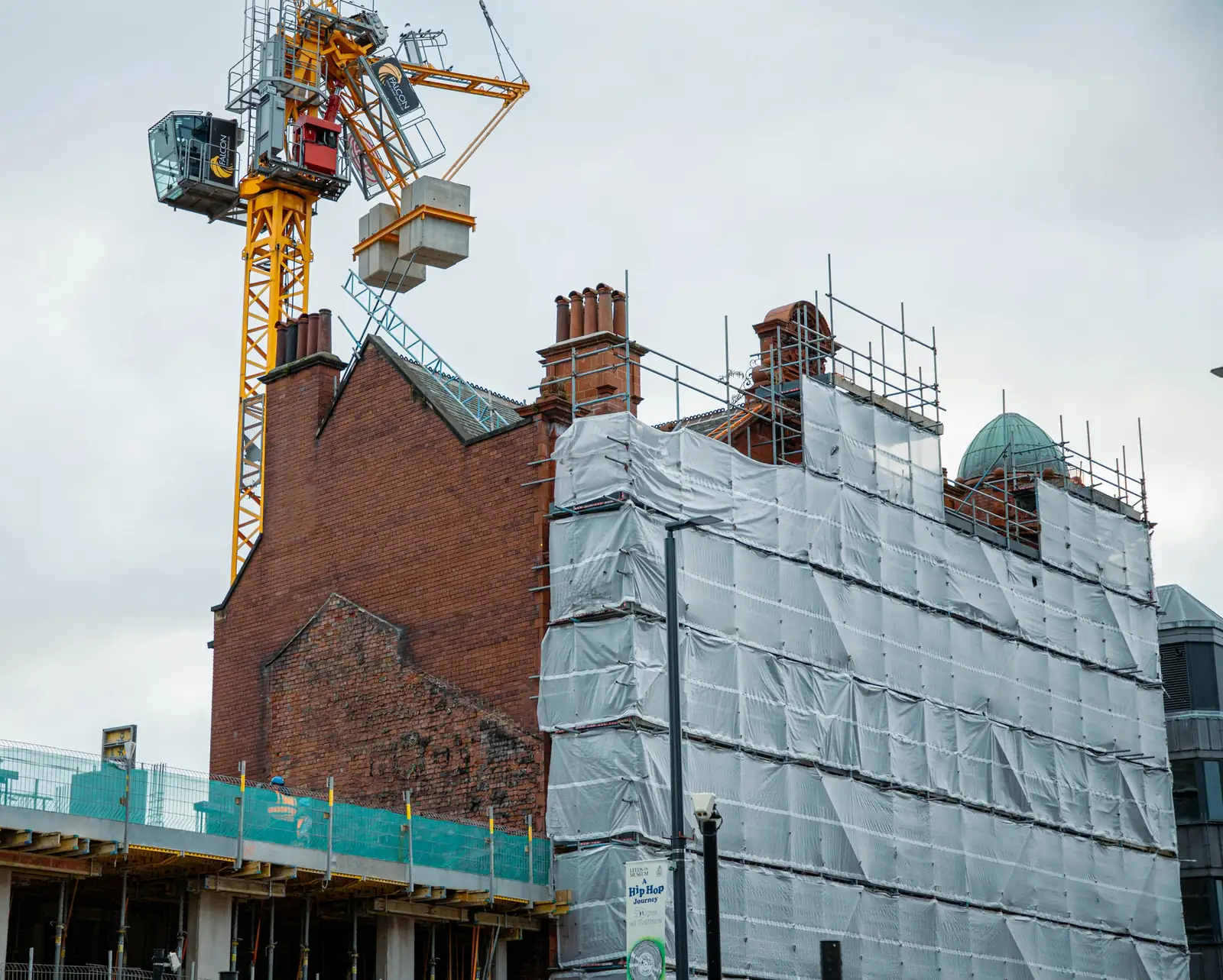 The tower crane's concrete counterweights hang above the chimney stacks of the old brick gable.