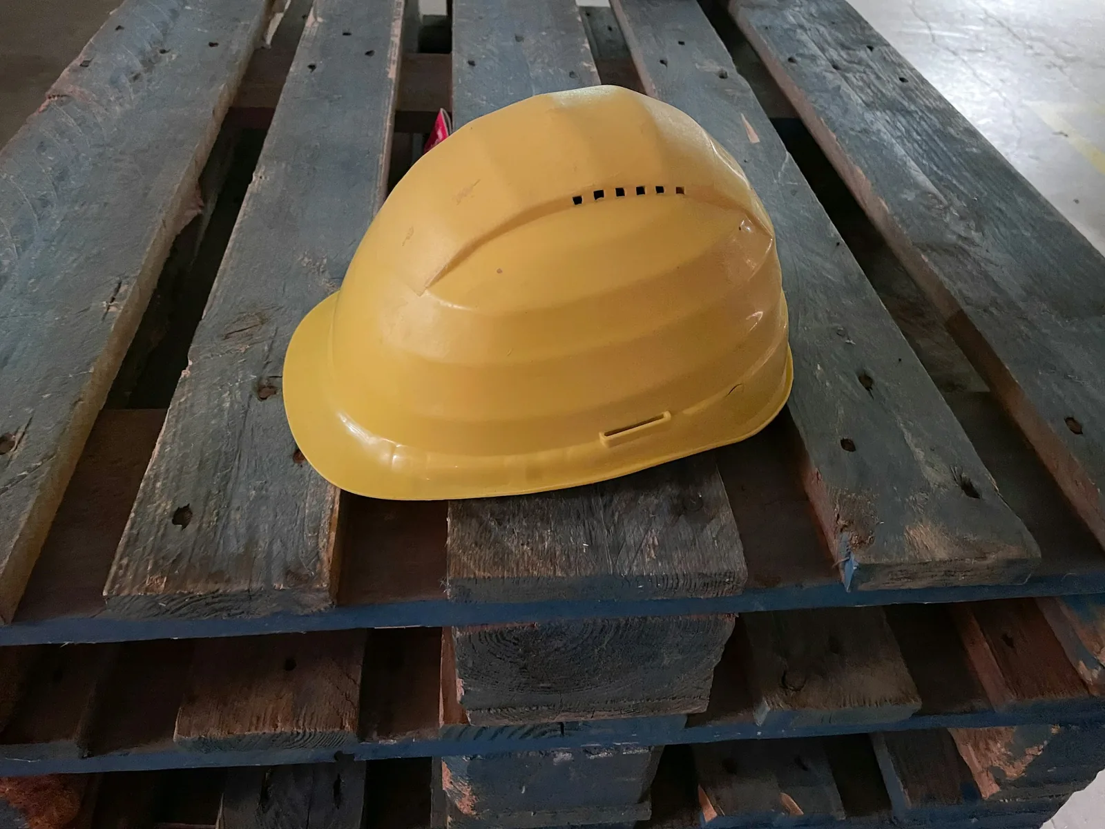 Someone has left a yellow hard hat on a stack of blue-painted timber pallets.