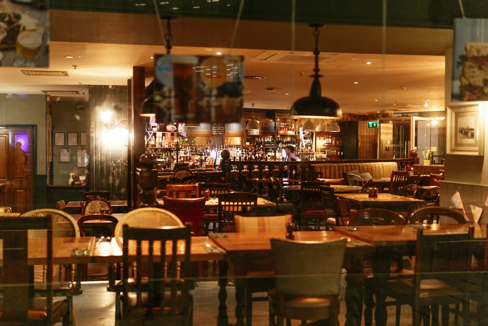 Timber tables and spindle-back chairs fill the floor, with the lit back bar beyond.
