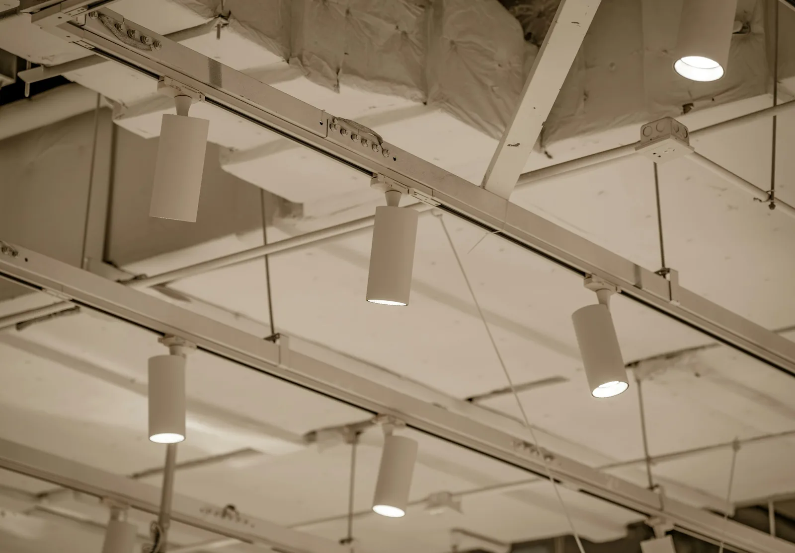 Cylinder spotlights are lit on their track while the ceiling grid above is still missing tiles.