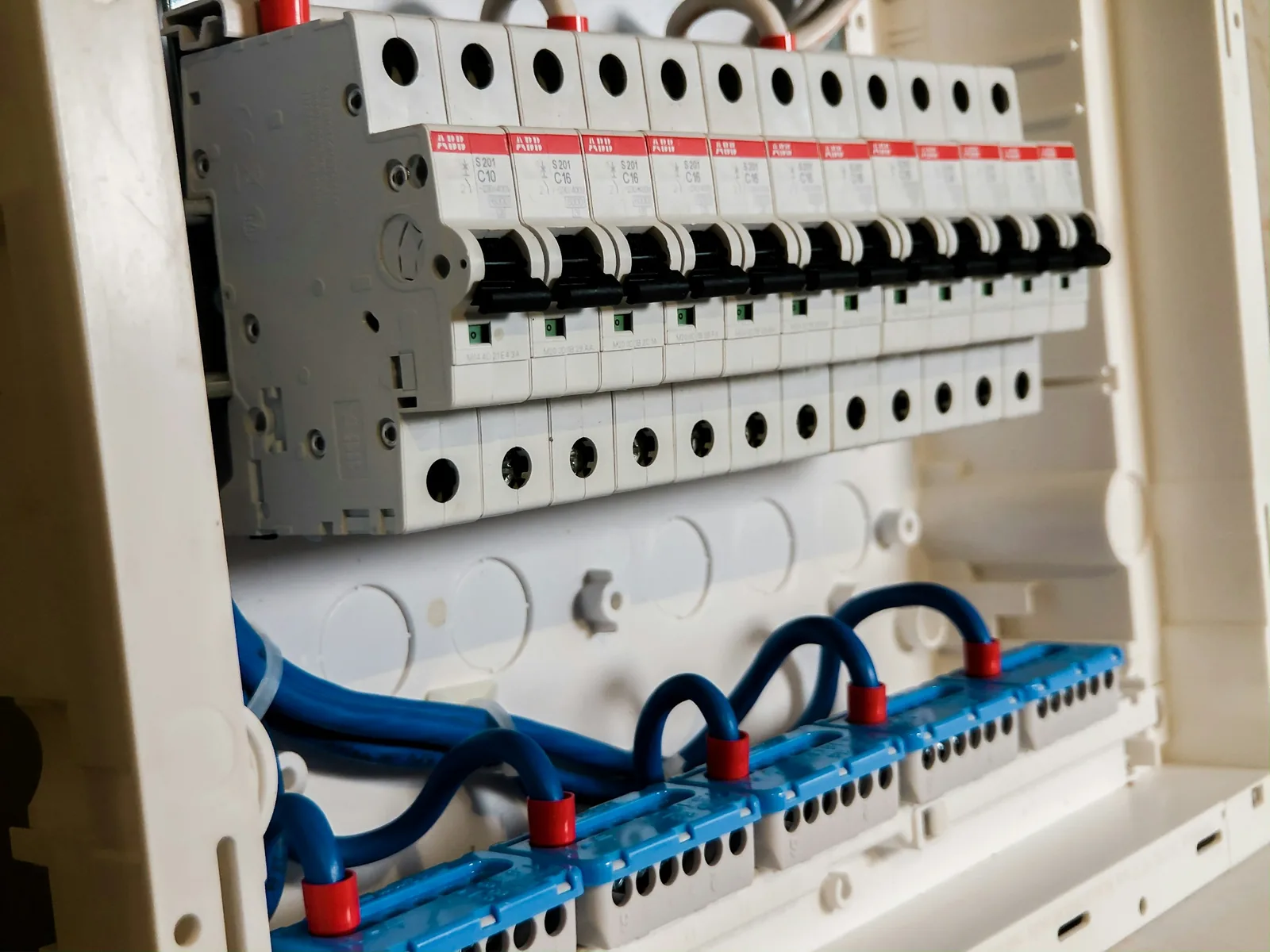 An opened consumer unit shows a rail of ABB breakers above blue neutral bars.