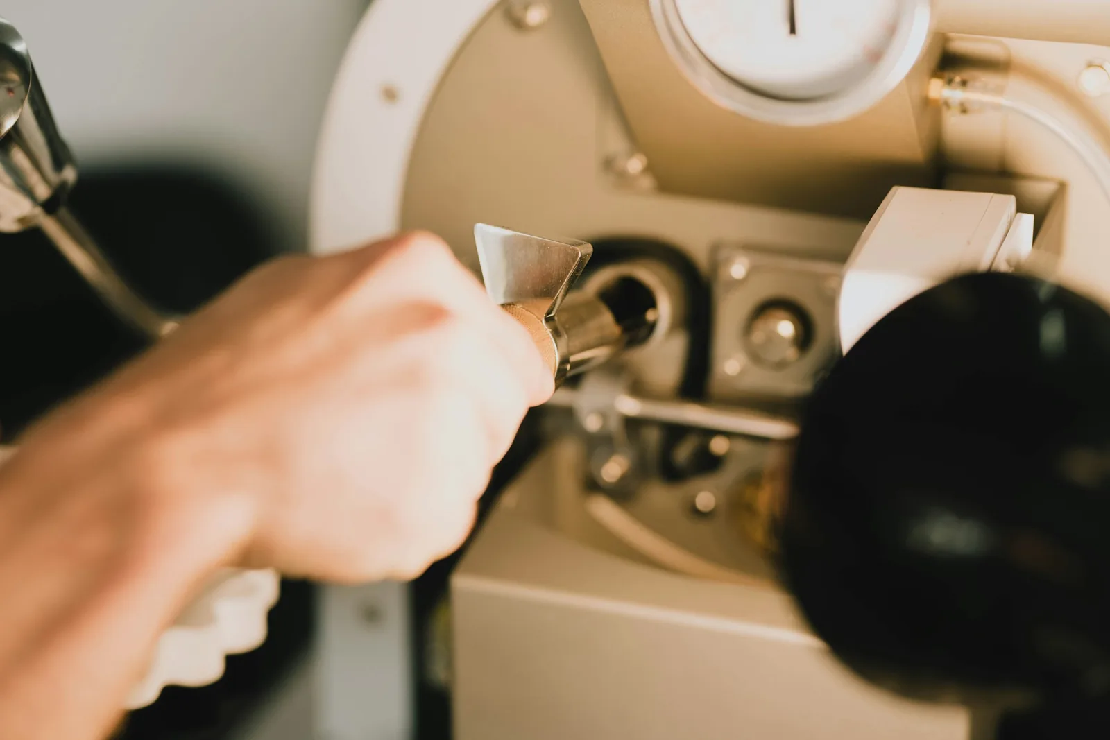 A hand pulls the chrome lever on a cream-panelled machine below a round dial gauge.