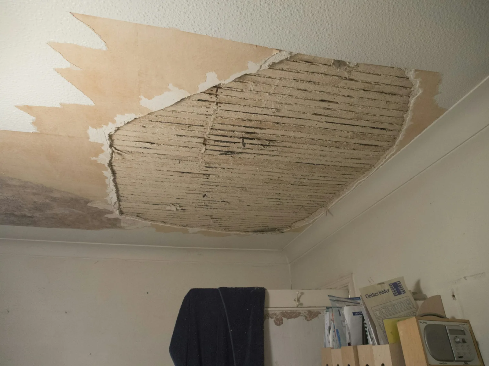 Ceiling plaster has come away to the bare timber laths, with water staining across the wallpaper.