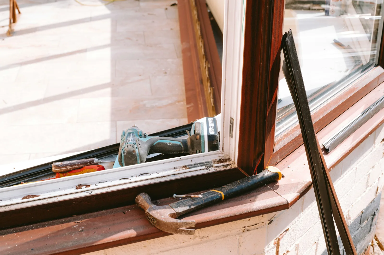 The drill sits in the window track and the hammer lies on the sill by a long screw.