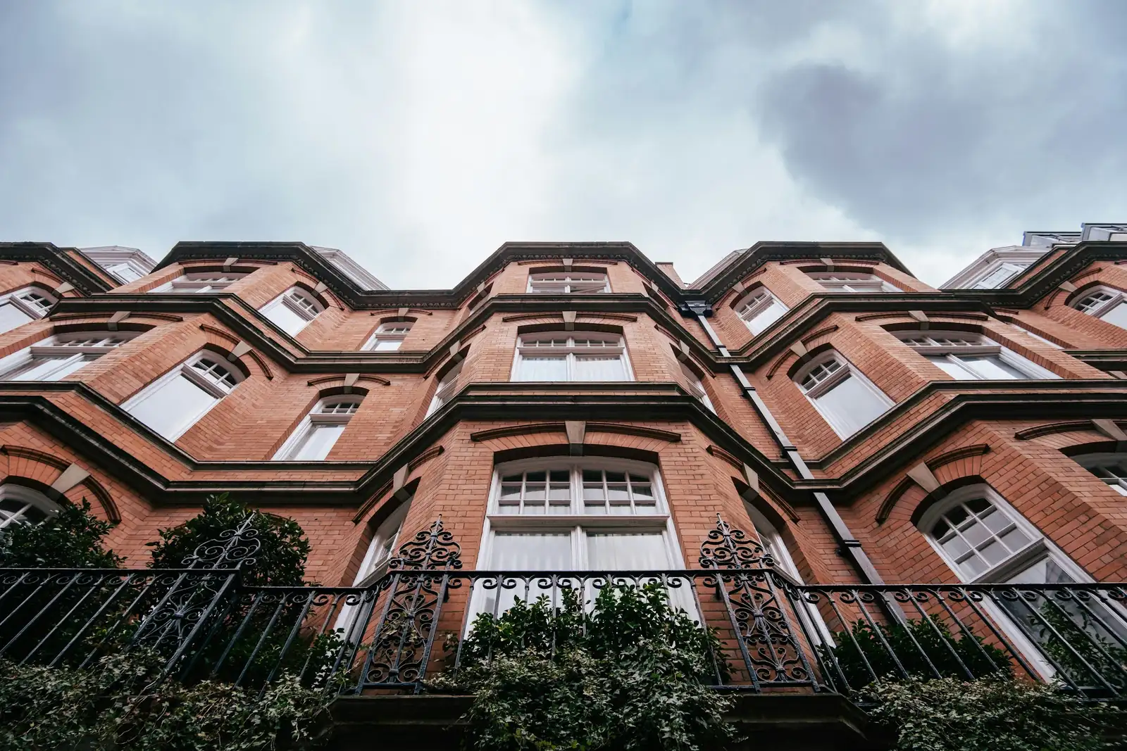 Seen from below, a red brick mansion block climbs past canted bays and iron balcony railings.