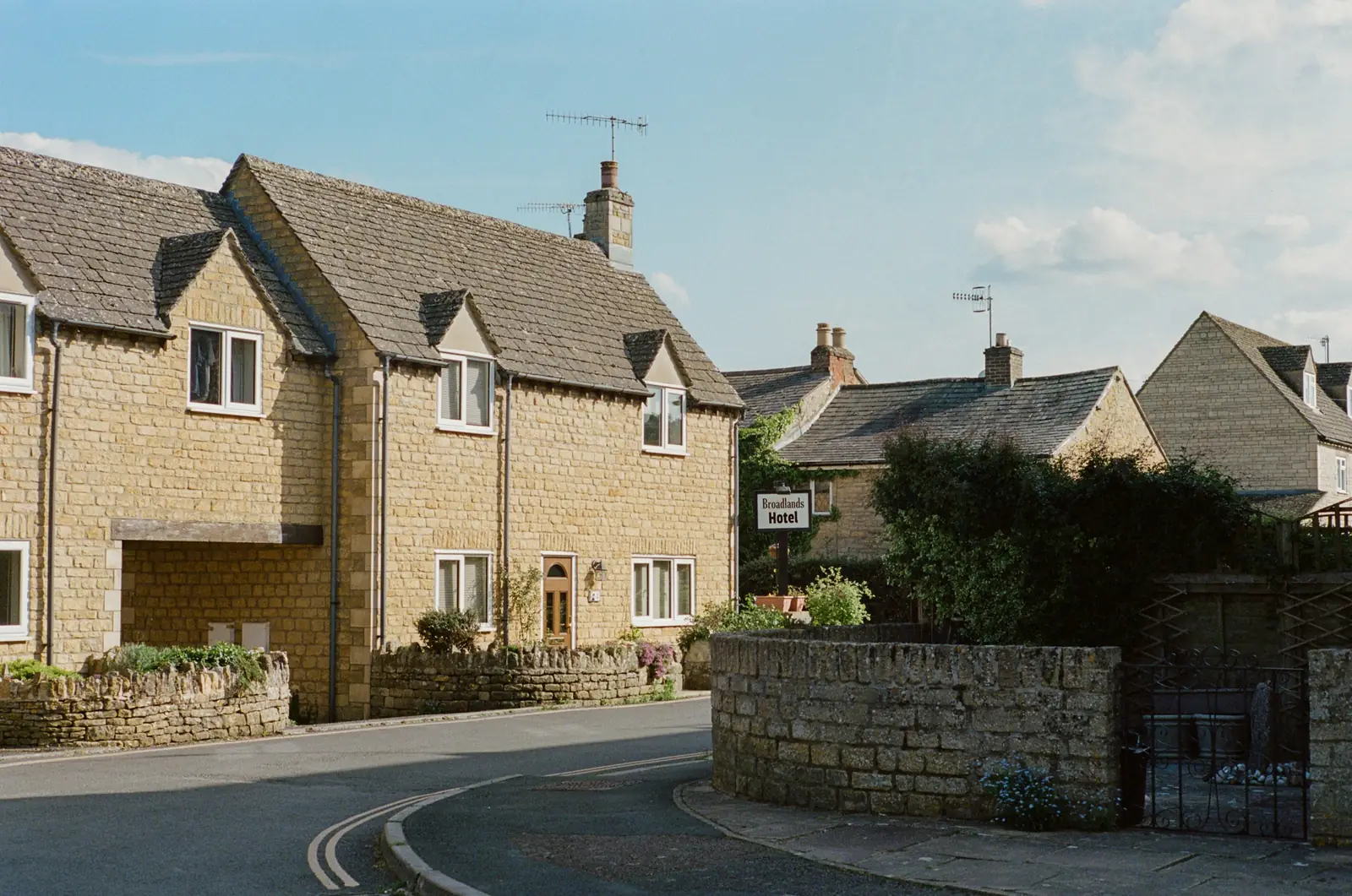 Honey-coloured stone under a stone-tiled roof, dry-stone walling with upright copings running down to the road.