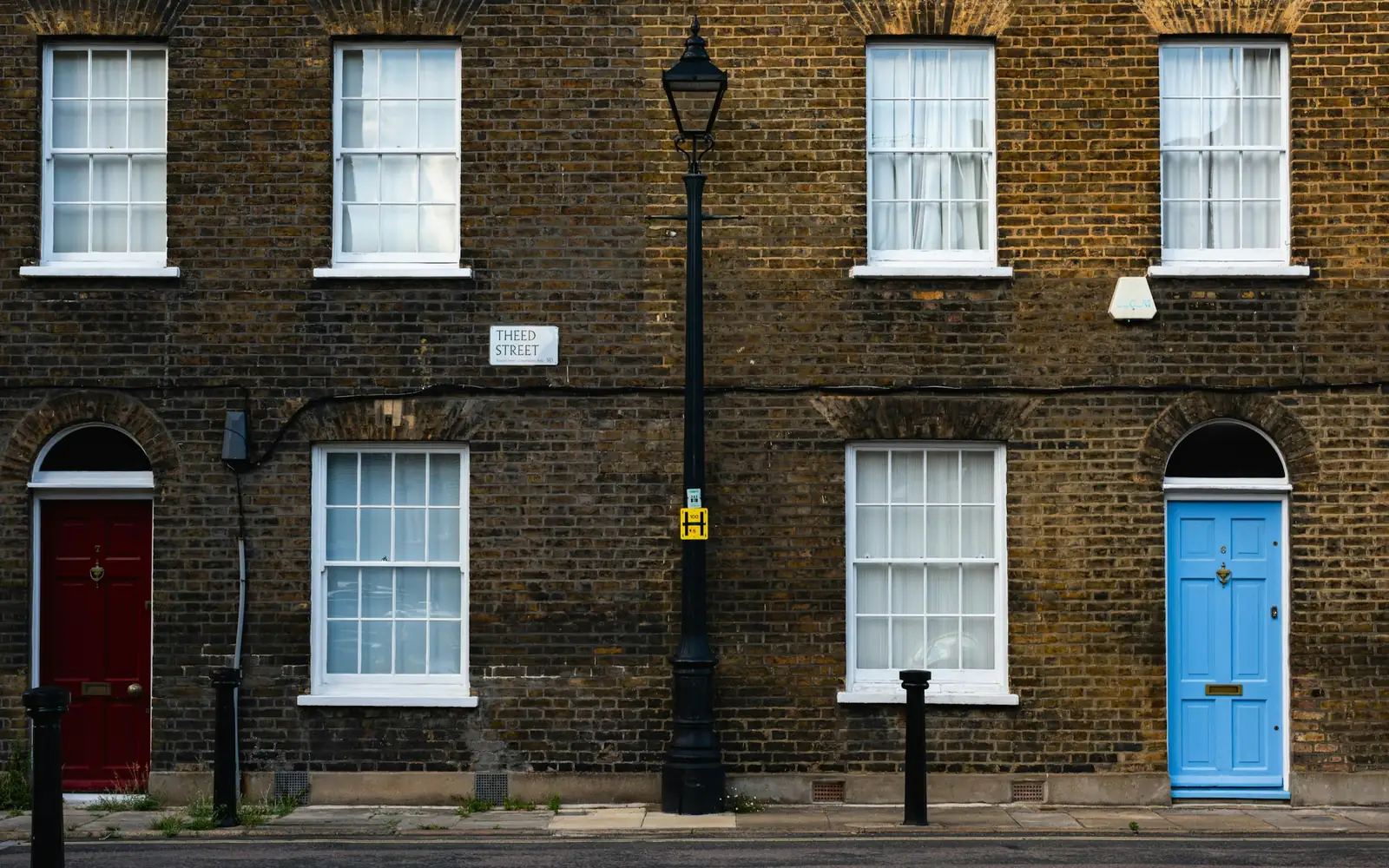 Two front doors, one red and one blue, in a yellow stock brick terrace with sash windows.