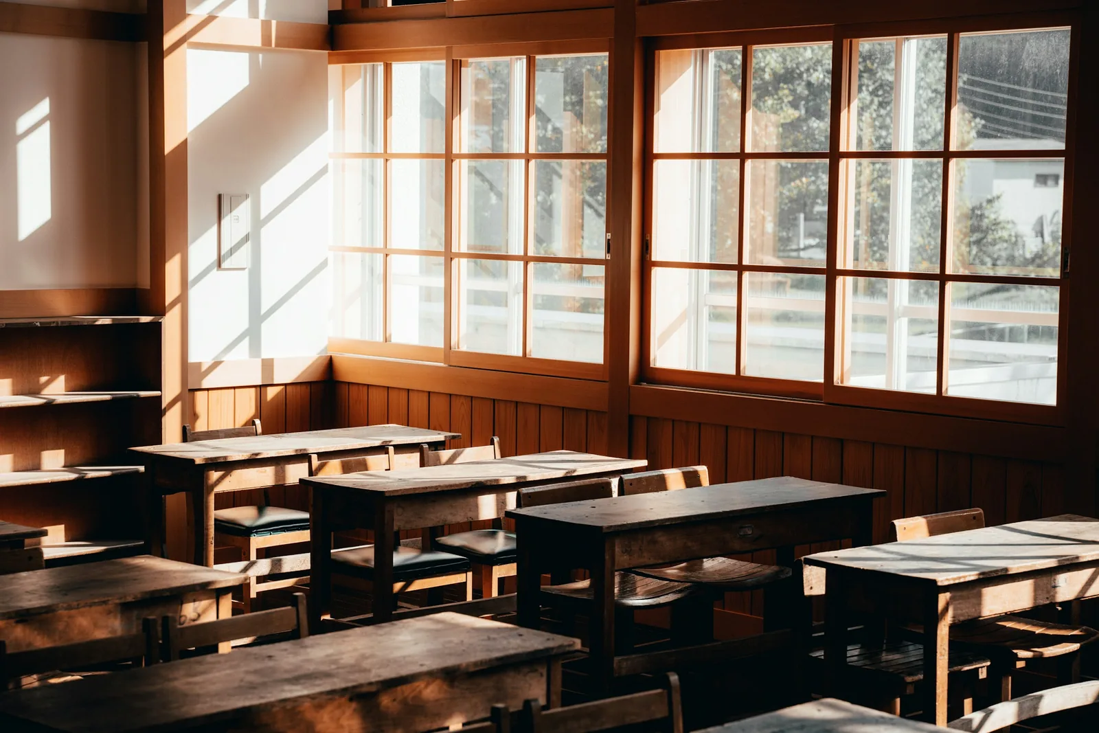 An empty classroom with timber desks and tall windows.