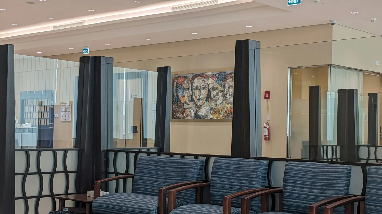 The waiting area holds one row of blue striped armchairs in front of glazed screens and dark clad columns.