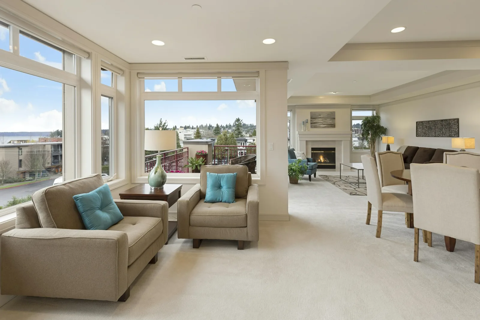 A beige sofa and armchair, each with a turquoise cushion, back onto the tall windows on pale carpet.