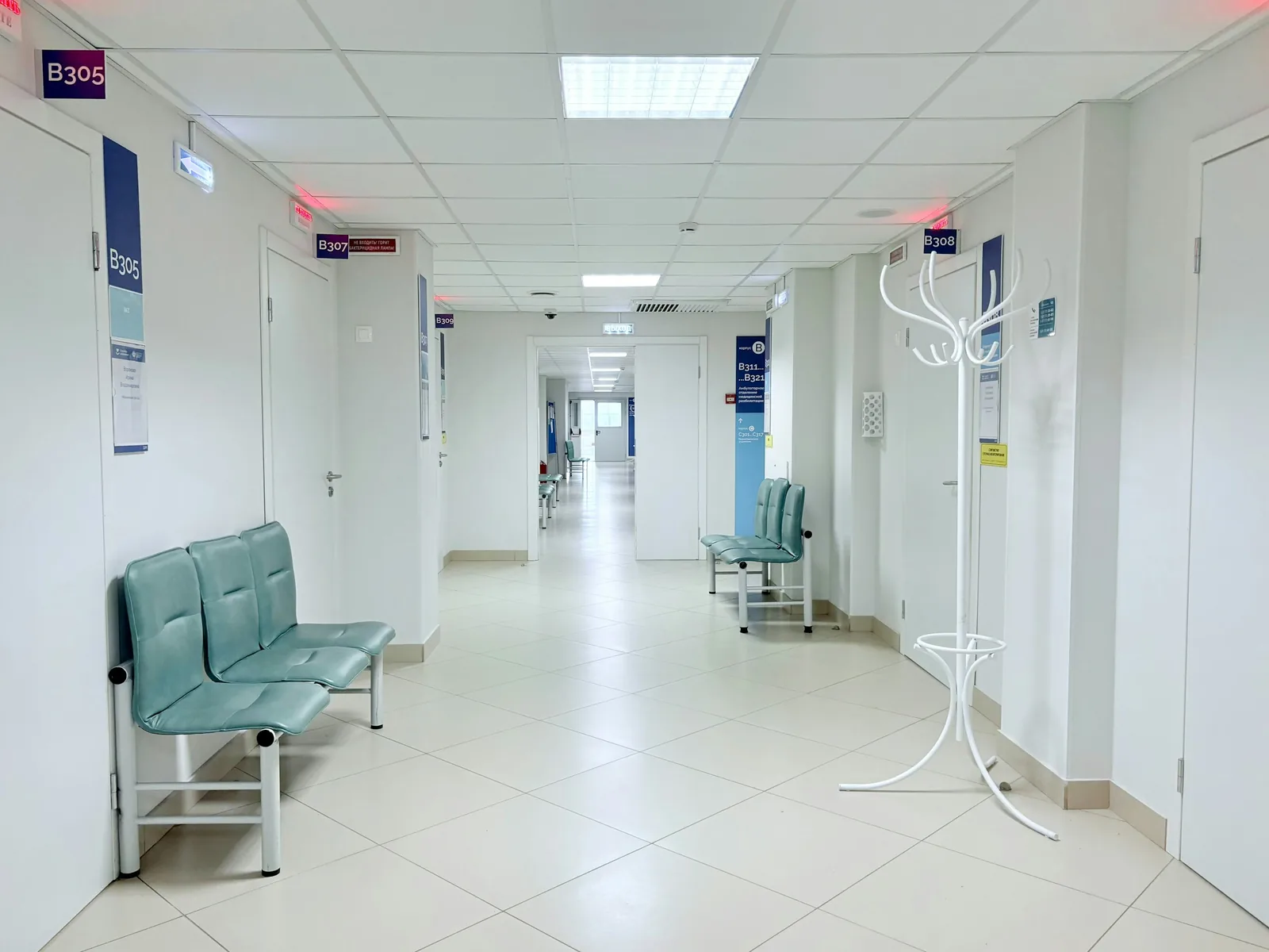 Down a white-tiled clinic corridor, mint vinyl benches sit beneath blue room-number signs.