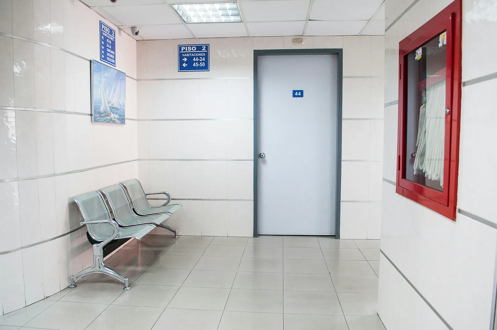 A steel bench sits against wall tiling carried to the ceiling, opposite a red fire hose cabinet.