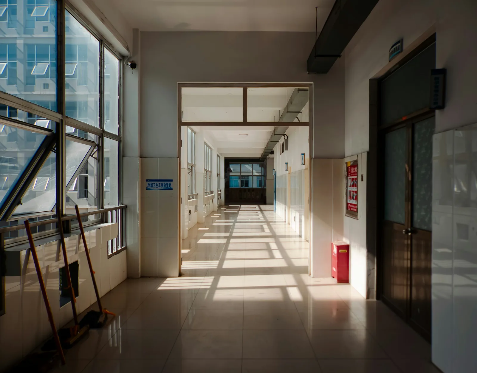 Sunlight falls in bars across a gloss-tiled corridor, mops leaning against the glazed wall.
