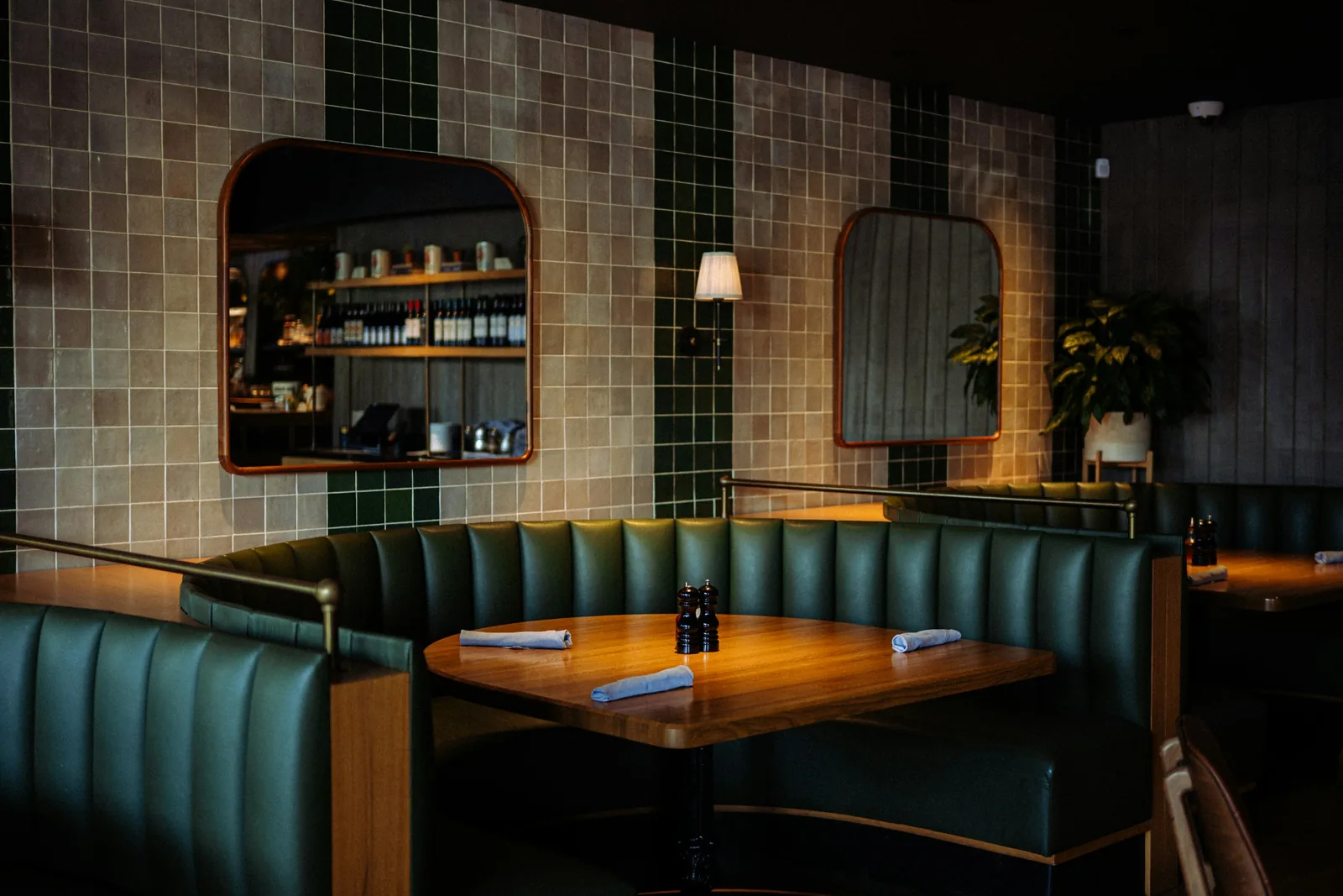 Fluted green banquettes curve round a timber table against a wall of stacked tile.
