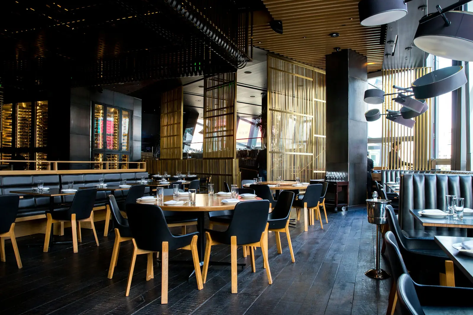 Floor-to-ceiling brass rod screens split the room, black chairs on pale timber legs, dark boards underfoot.