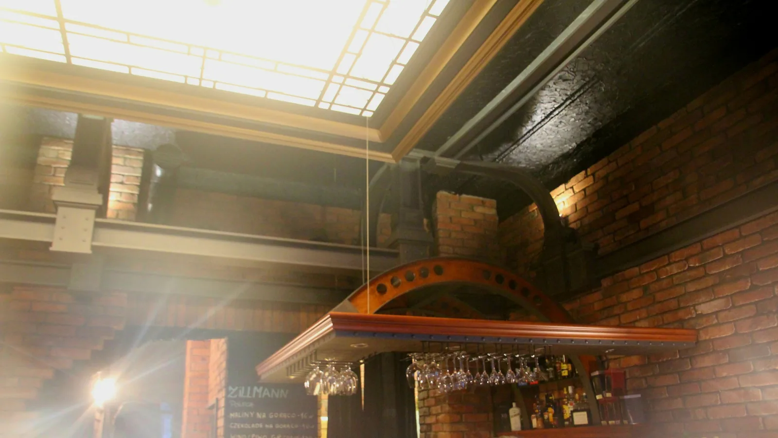 Wine glasses hang from a suspended timber rack below painted ironwork and exposed brick.