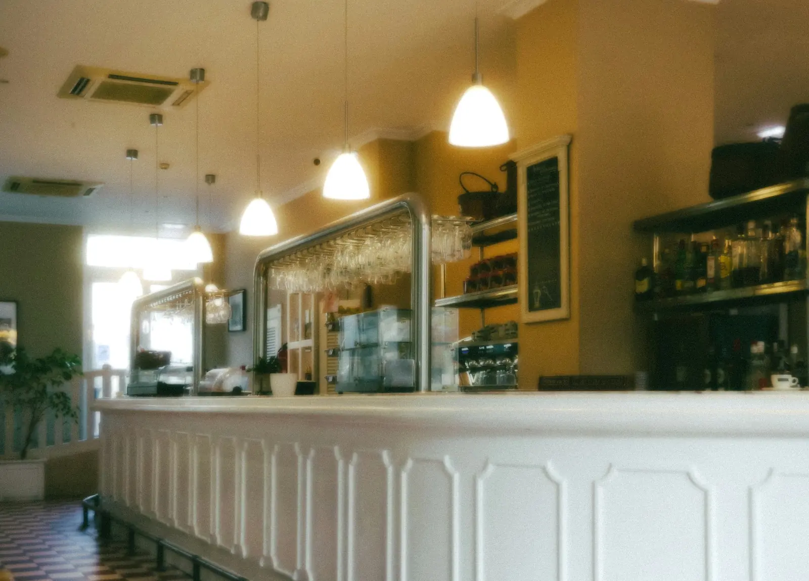 The long counter front is moulded white panelling, glasses racked on steel tube above.
