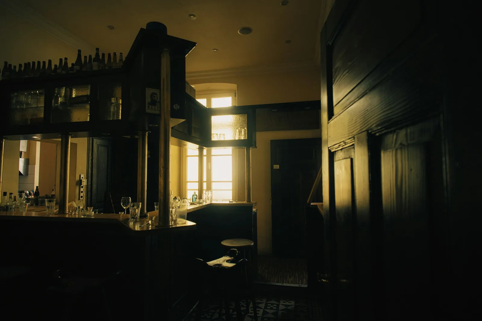 Late sun comes through the window onto a timber counter, its glazed cabinet carried on brass columns.
