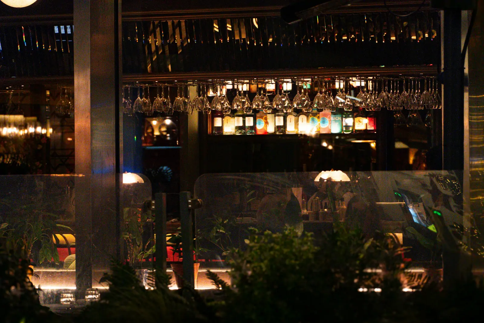 Rows of wine glasses hang above a back bar of lit bottles in a high-end cocktail bar.