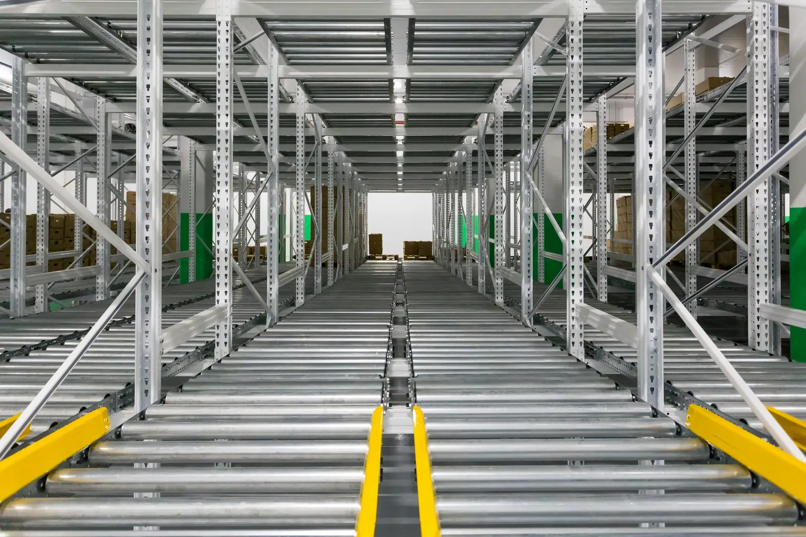 Galvanised pallet racking with roller lanes and yellow guides, installed in an empty warehouse.