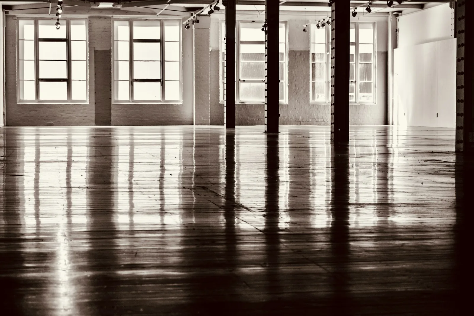 An older industrial space cleared back to its columns, with tall windows reflected in a newly sealed floor.